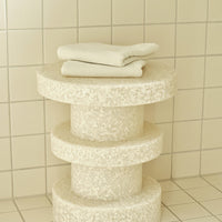 Stylish creamy white three-tier stool with a textured finish, featuring neatly stacked white towels.