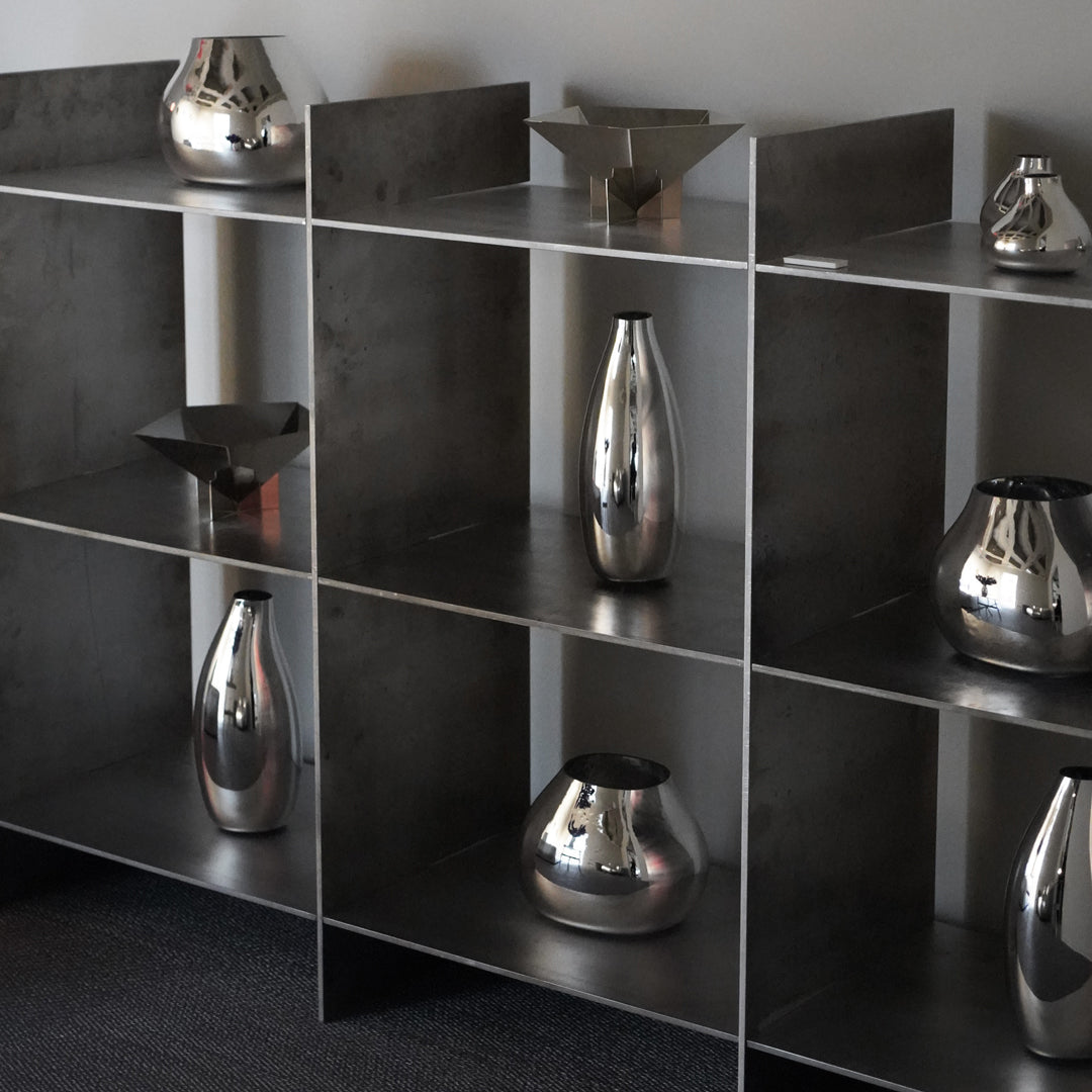 Silver vases in a modern black shelving unit, showcasing sleek designs and reflective surfaces.