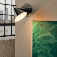 Modern chrome wall sconce illuminating a vibrant green abstract painting with fluid brushstrokes.