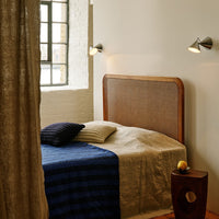 Cozy bedroom featuring a light beige bedspread, blue striped blanket, and neutral-toned curtains. Warm wooden accents.
