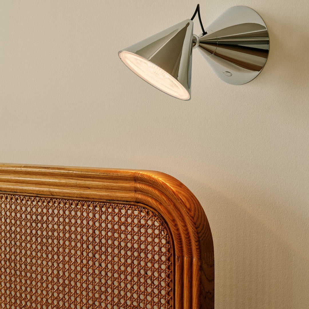 Sleek chrome wall lamp with a conical shade, paired with a warm-toned rattan headboard featuring a woven pattern.