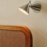 Sleek chrome wall lamp with a conical shade, paired with a warm-toned rattan headboard featuring a woven pattern.