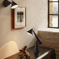 Black modern lamp with geometric design, paired with neutral-toned decor and soft lighting against a brick wall.