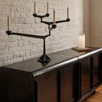 Black candelabra on a dark wood console against a textured white brick wall, creating a modern and minimalist aesthetic.