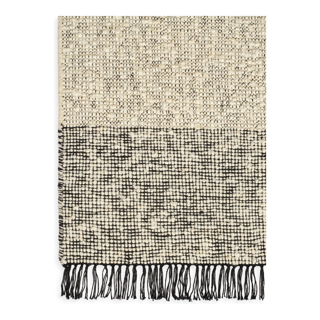 Textured beige and black patterned throw blanket with fringed edges.
