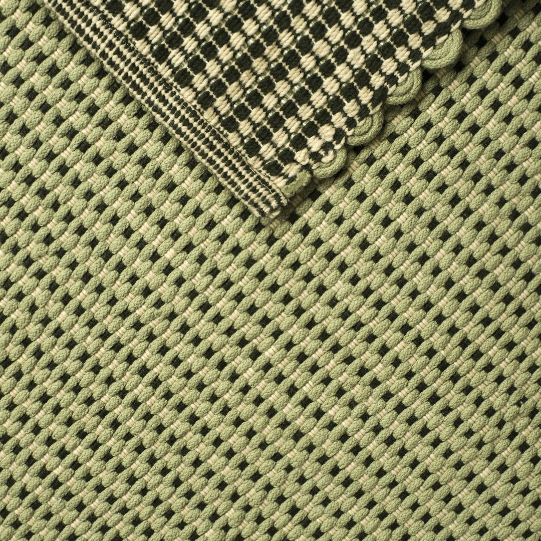 Green woven fabric with a black and cream checkered pattern and scalloped edge detail.