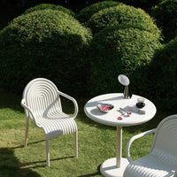 White striped outdoor chairs and round table in a lush green garden setting.