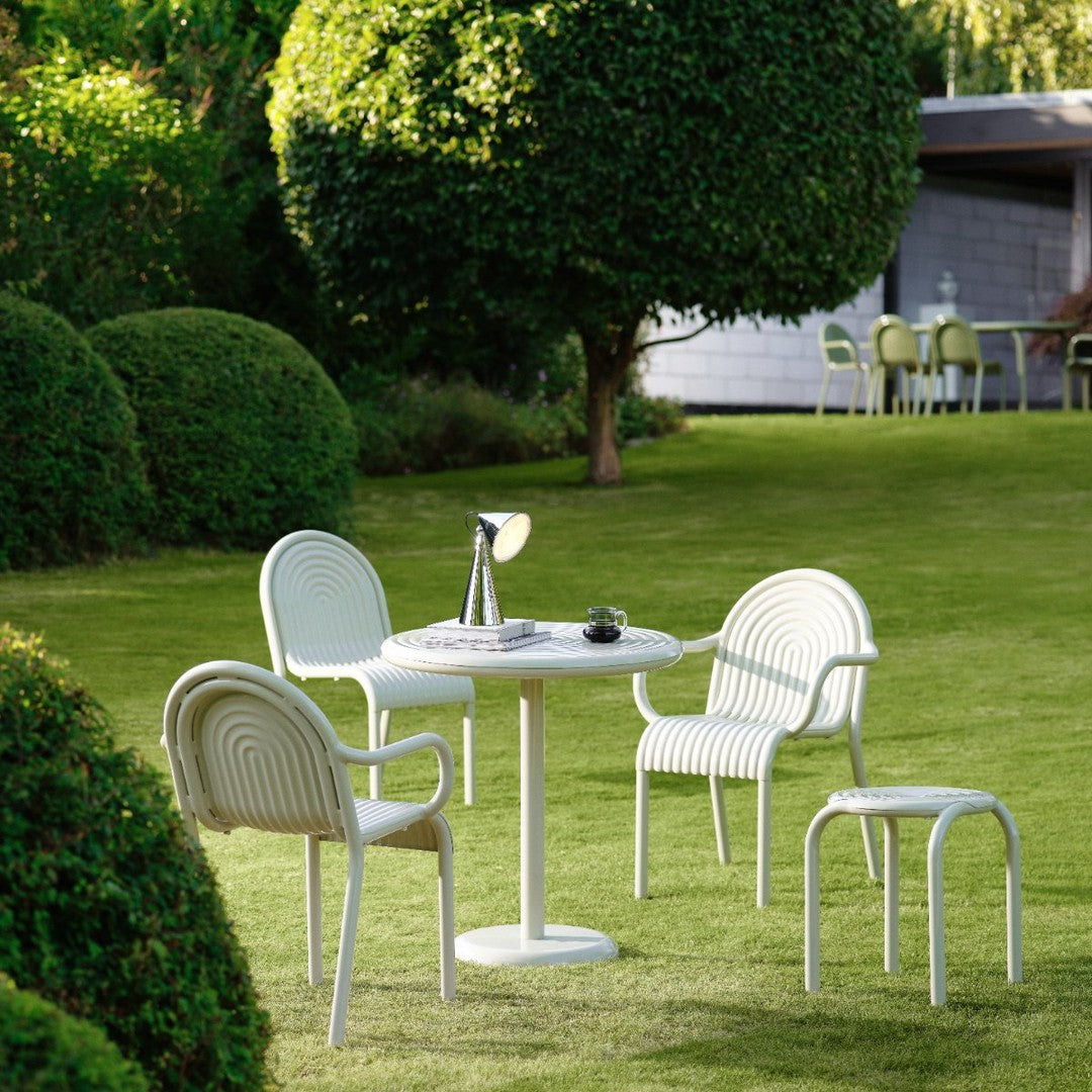 Modern outdoor table and four white chairs, featuring curved lines, set against a lush green lawn and vibrant hedges.