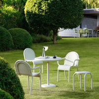 Modern outdoor table and four white chairs, featuring curved lines, set against a lush green lawn and vibrant hedges.