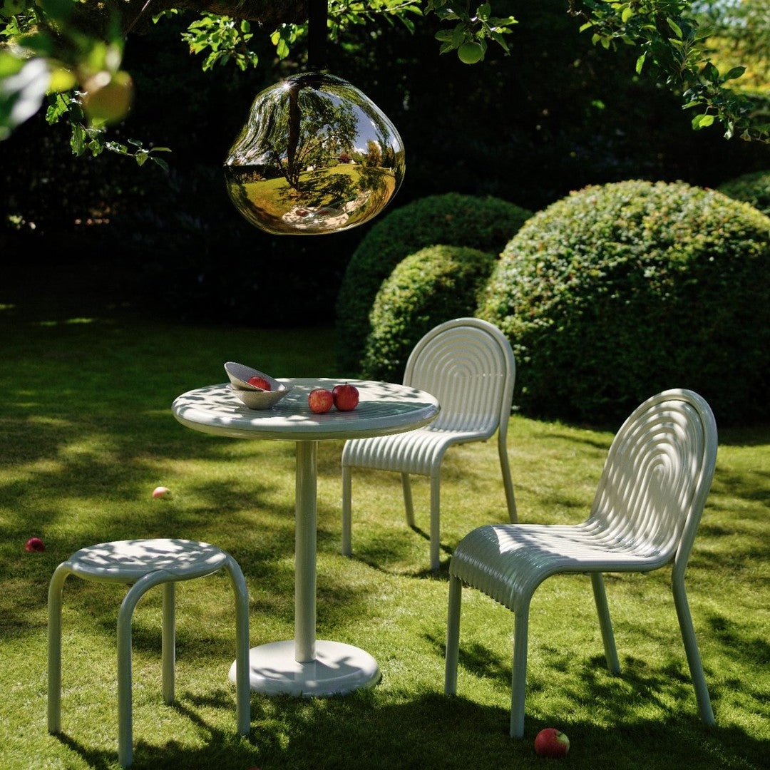 Stylish white outdoor furniture with subtle ribbed patterns, set against lush green shrubs in a sunny garden.