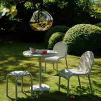 Stylish white outdoor furniture with subtle ribbed patterns, set against lush green shrubs in a sunny garden.