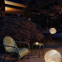 "Green woven chair and table set against a dark backdrop, featuring soft glowing lanterns."