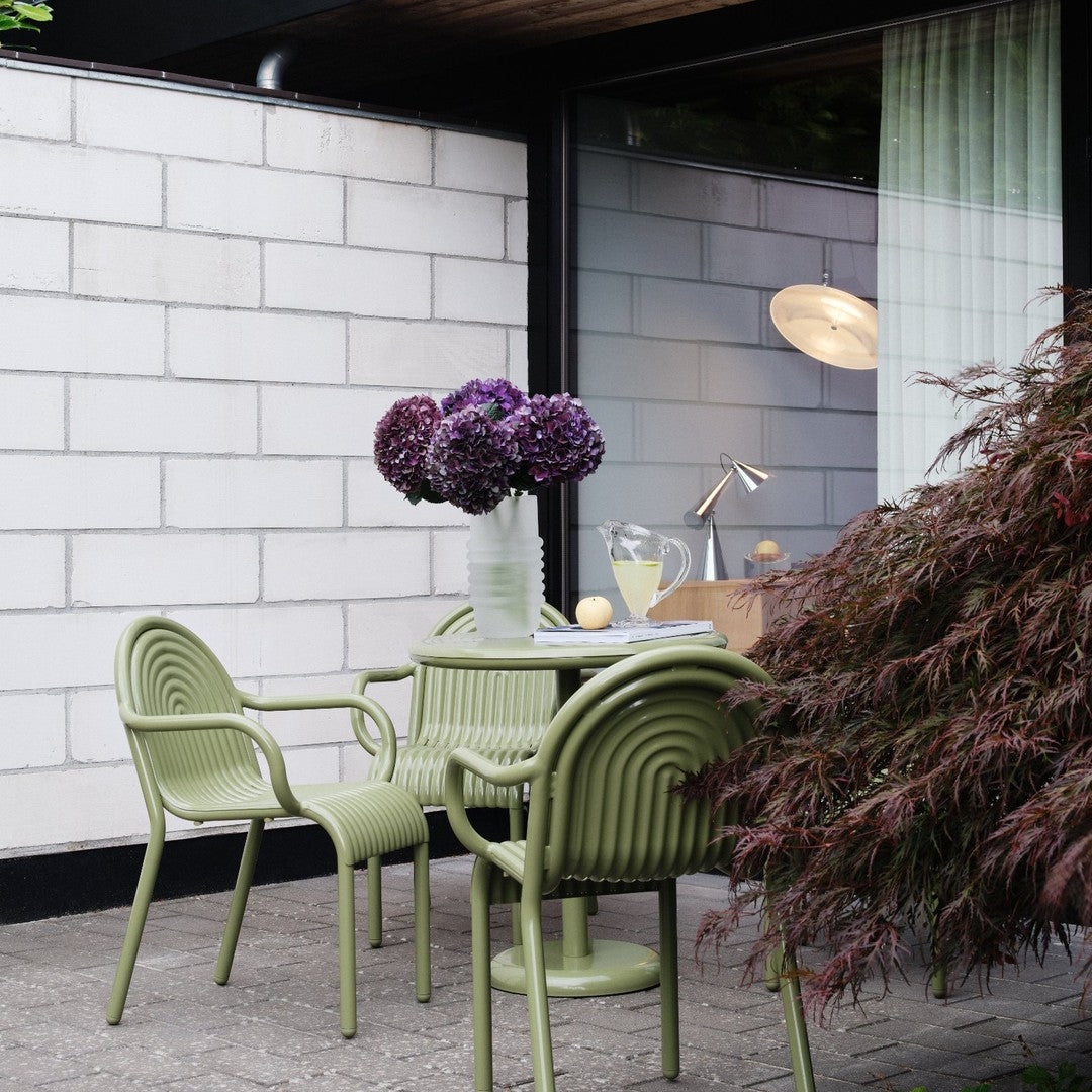 Green ribbed outdoor chairs and table, complemented by purple flowers against a minimalist backdrop. Stylish modern design.
