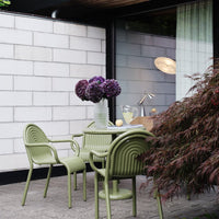 Green ribbed outdoor chairs and table, complemented by purple flowers against a minimalist backdrop. Stylish modern design.