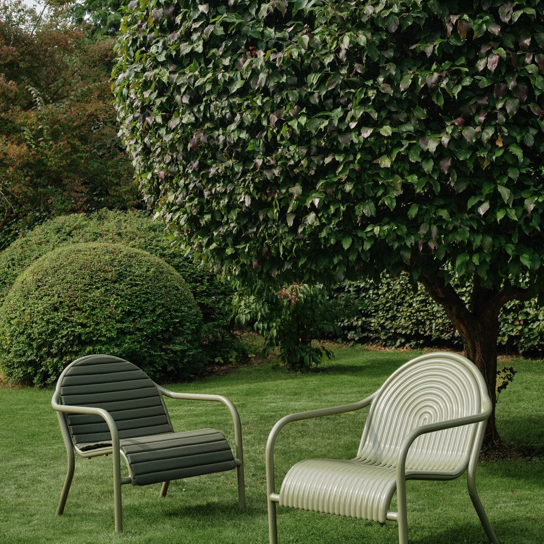 Two outdoor chairs in olive green and cream, featuring striped and smooth patterns, set in a lush garden.