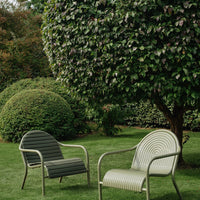 Two outdoor chairs in olive green and cream, featuring striped and smooth patterns, set in a lush garden.