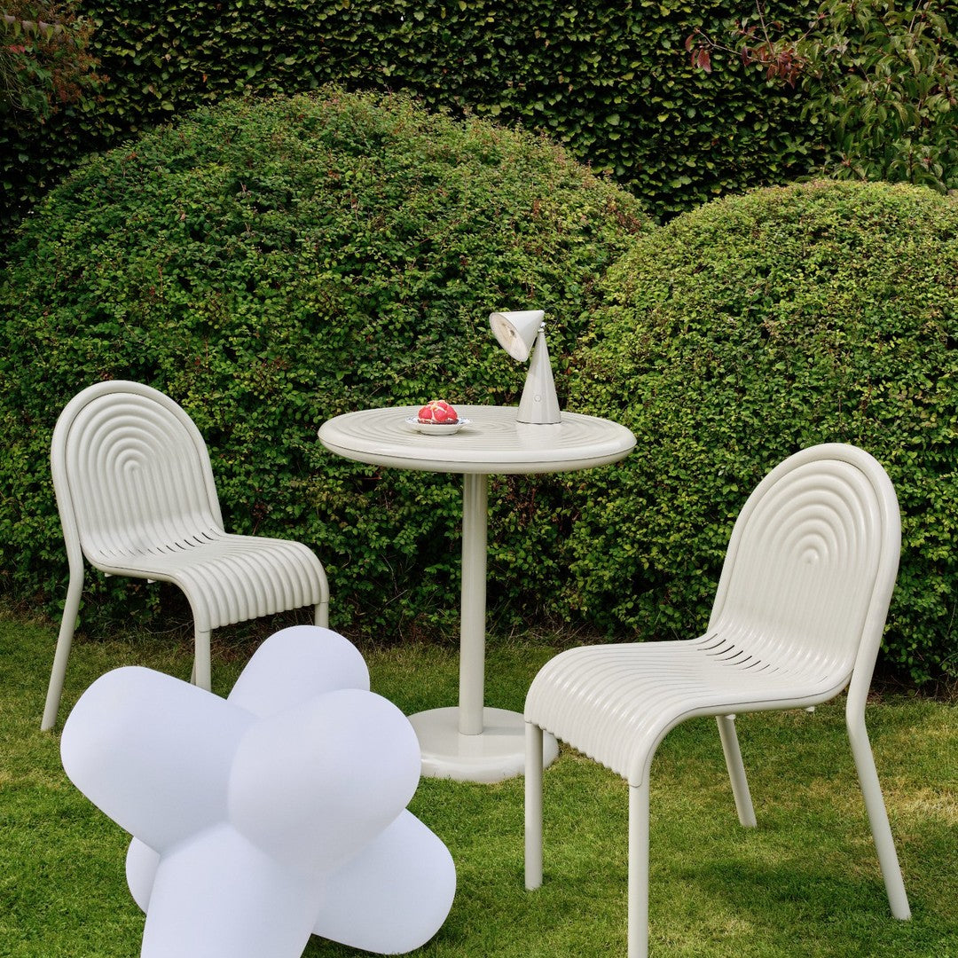 White outdoor chairs and table, featuring curved lines and a smooth finish, complemented by lush green foliage.