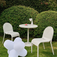 White outdoor chairs and table, featuring curved lines and a smooth finish, complemented by lush green foliage.
