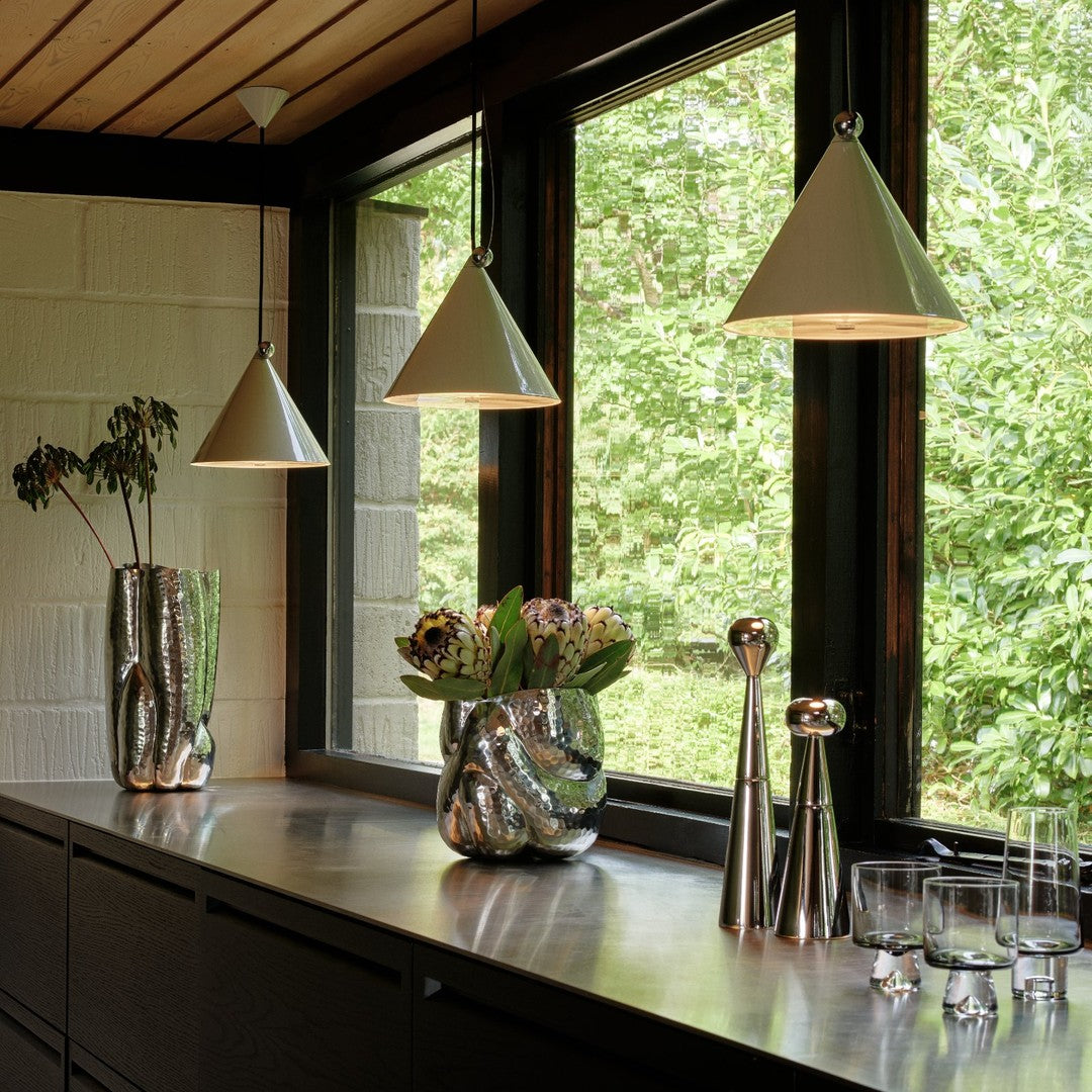 Modern kitchen featuring sleek silver accents, geometric white lampshades, and fresh greenery against dark wood elements.