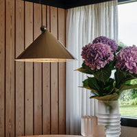 "Gold conical pendant light above white vase with vibrant purple hydrangeas against wood-paneled wall."