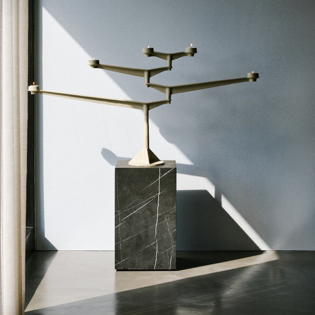 Gold geometric candle holder on a textured dark stone base, set against a light grey wall with soft shadows.