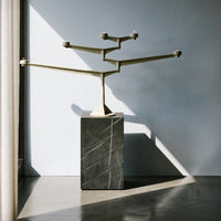 Gold geometric candle holder on a textured dark stone base, set against a light grey wall with soft shadows.