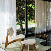 Soft white curtains, natural wood furnishings, and a green patterned rug create a serene, modern living space.