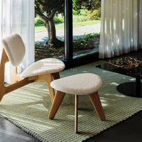 White textured upholstery on modern chairs and stool, set against a pale green woven rug in a bright, airy interior. 