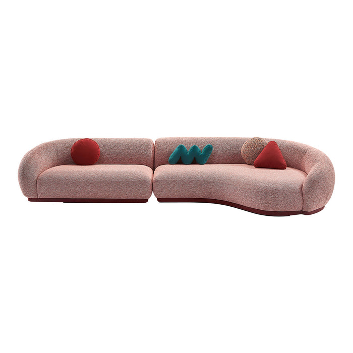 Curved sofa in soft pink fabric, accented with vibrant teal, red, and textured pillows showcasing geometric patterns.