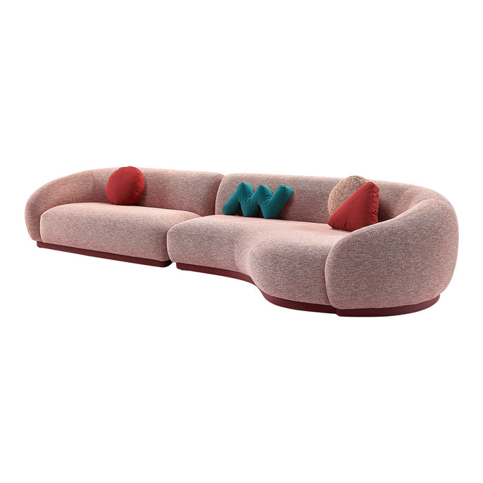 Curved sofa in soft pink fabric, accented with teal and red cushions, featuring a sleek maroon base and subtle texture.