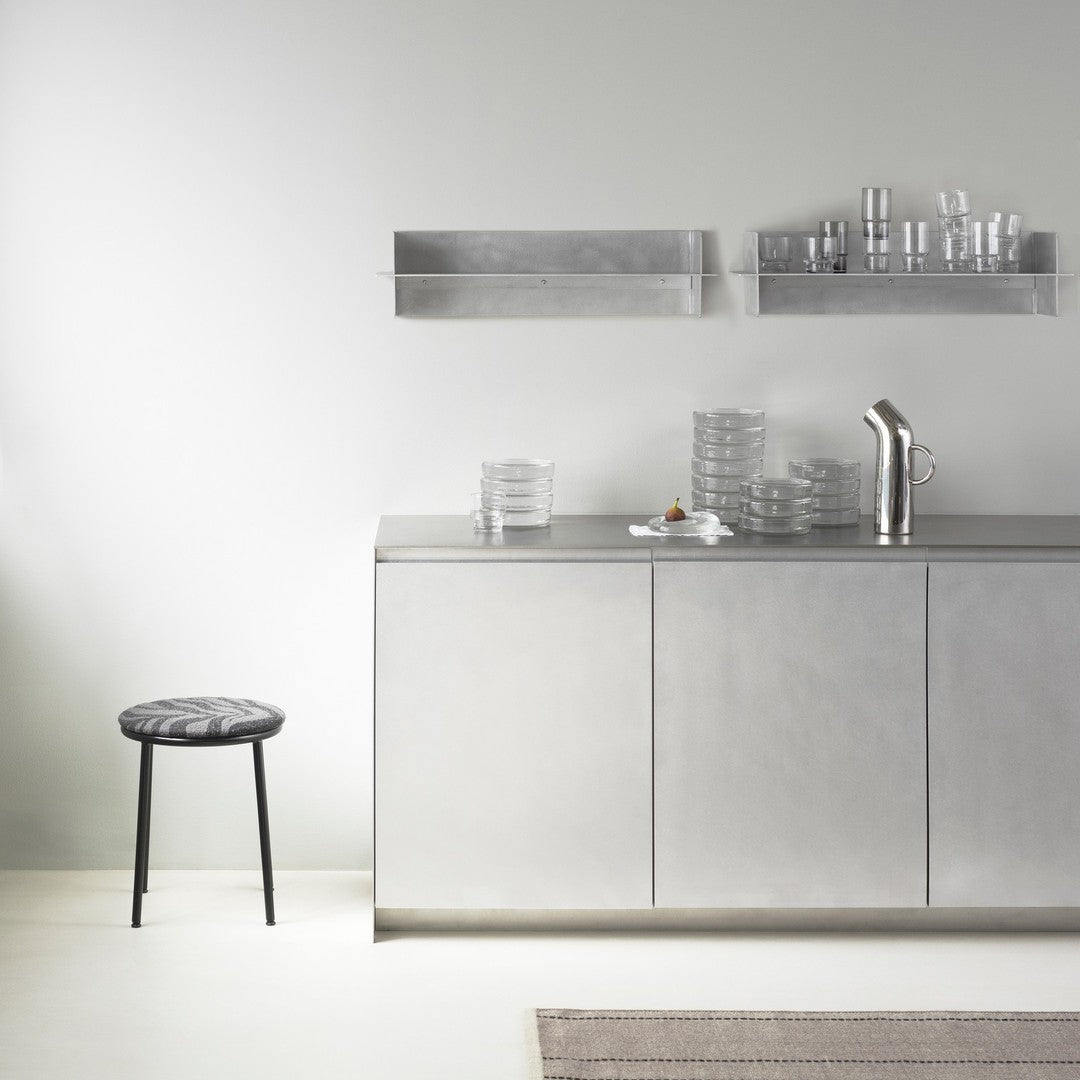 Modern kitchen scene featuring sleek silver metallic surfaces and a patterned gray stool. Clear glassware contrasts elegantly.