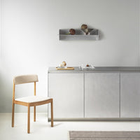 Light beige chair with wooden legs, silver cabinet, and grey wall; soft textures and minimalist design.