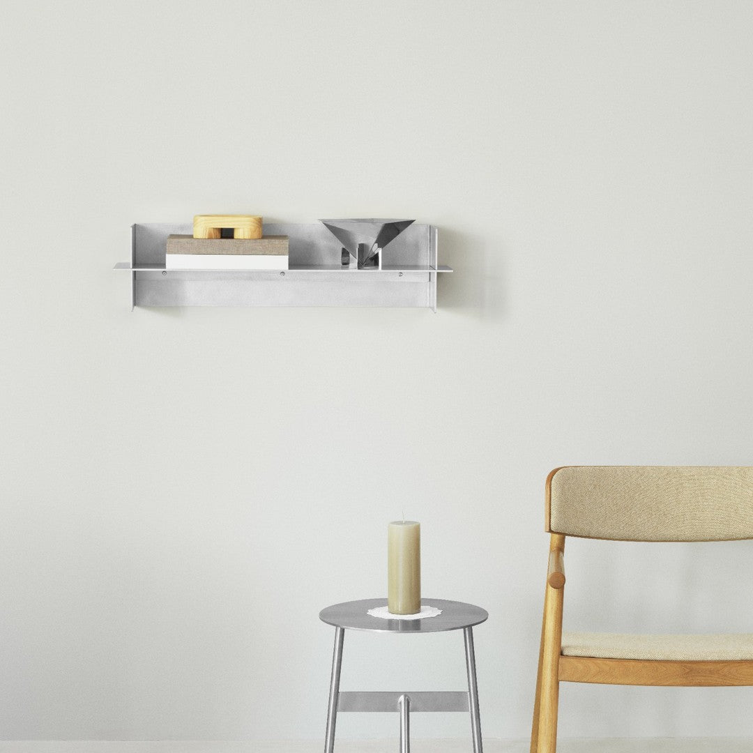 Silver wall shelf displaying wooden and white items against a light gray wall, paired with a round silver table and beige chair.