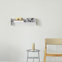 Silver wall shelf displaying wooden and white items against a light gray wall, paired with a round silver table and beige chair.