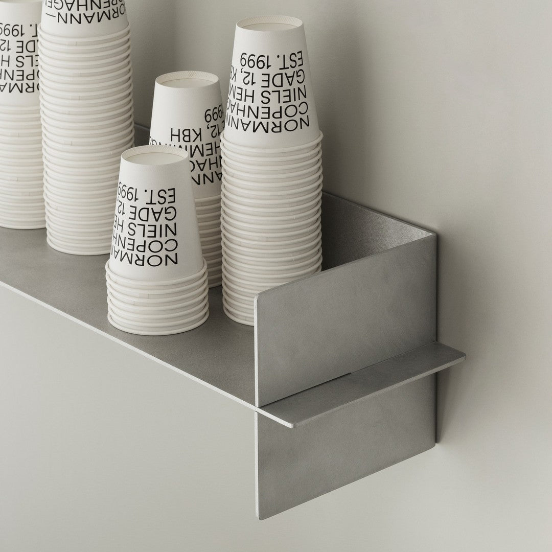 Stacked white cups with black text on a gray, minimalist shelf against a neutral wall. Clean and modern design.
