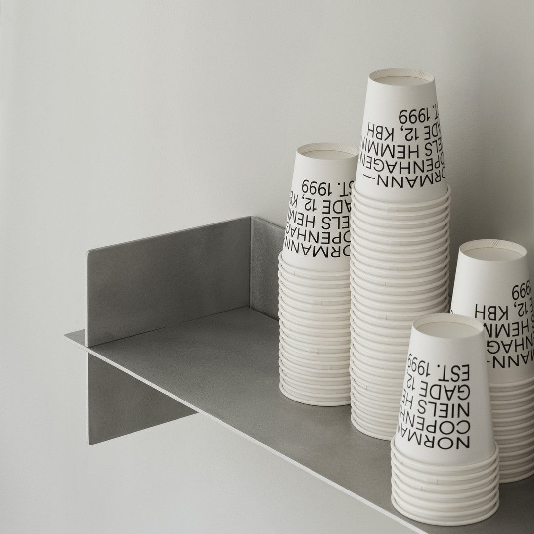 Stacked white cups with black text on a minimalist gray shelf against a light background.