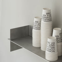 Stacked white cups with black text on a minimalist gray shelf against a light background.