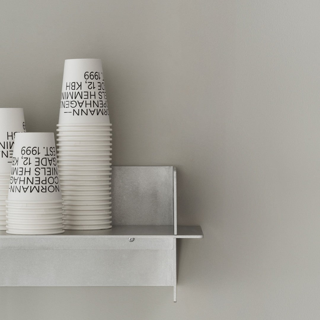 White paper cups with black text stacked on a gray shelf against a smooth gray wall. Minimalist design, modern aesthetic.