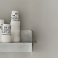 White paper cups with black text stacked on a gray shelf against a smooth gray wall. Minimalist design, modern aesthetic.