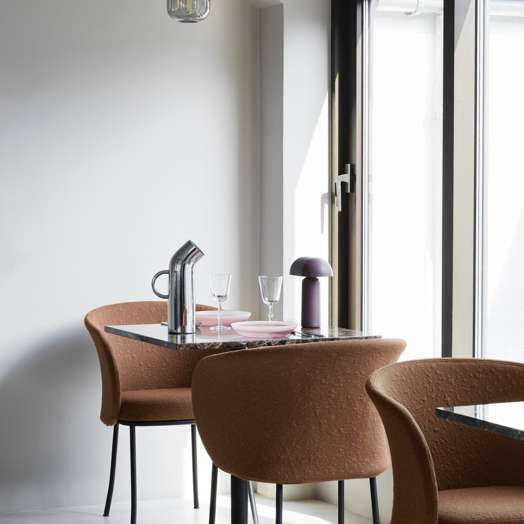 Modern dining setup featuring brown upholstered chairs, a black marble table, and soft pink dishes with a purple lamp.