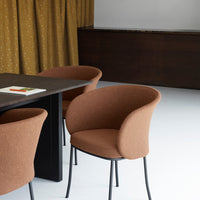 Rust-colored upholstered chairs with a textured finish against a sleek black table and golden patterned curtains.