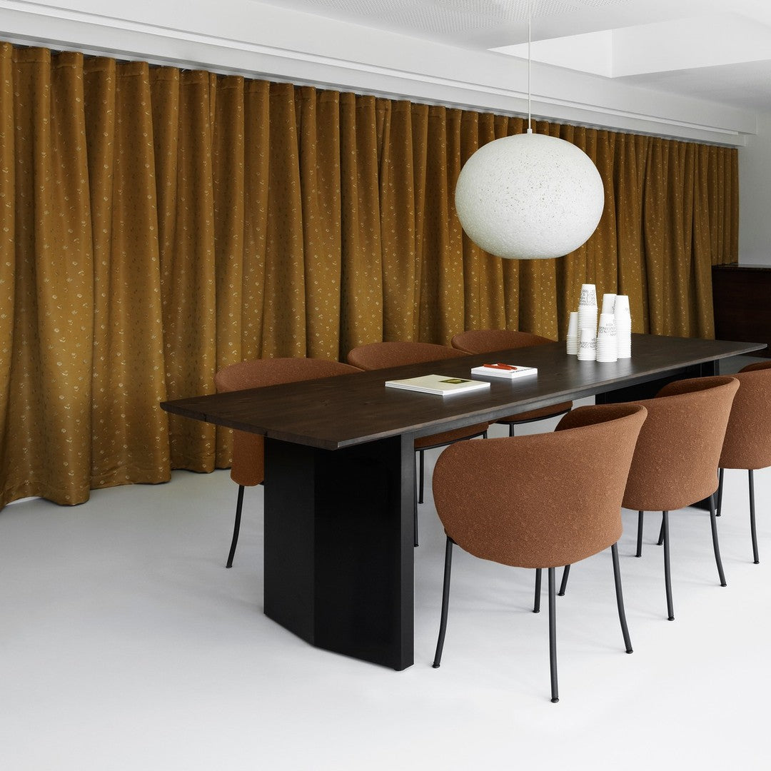 Brown patterned curtains and rust-colored chairs complement a sleek black table in a modern dining space.