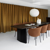 Brown patterned curtains and rust-colored chairs complement a sleek black table in a modern dining space.