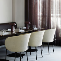 Beige upholstered chairs with black bases, dark brown marble table, and soft purple sheer curtains create a modern dining scene.