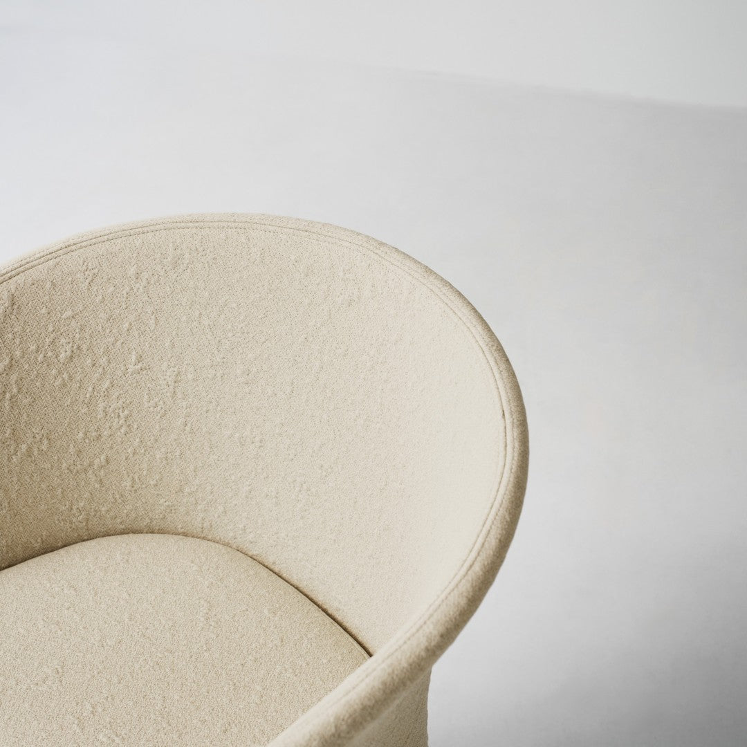 Beige upholstered armchair with a soft, textured fabric, featuring a smooth circular shape and neutral tones.