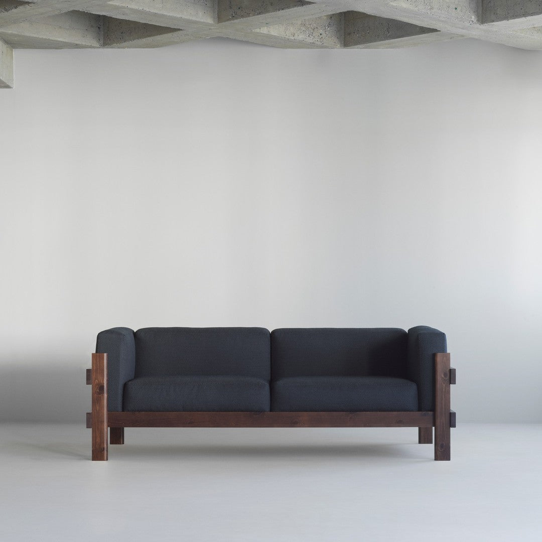 Modern dark gray sofa with a textured fabric and rich brown wooden frame, set against a minimalist backdrop.