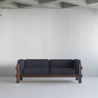 Modern dark gray sofa with a textured fabric and rich brown wooden frame, set against a minimalist backdrop.