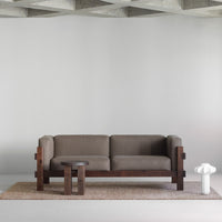Brown fabric sofa with dark wood frame, paired with a round wooden table on a textured beige rug. Minimalist style.