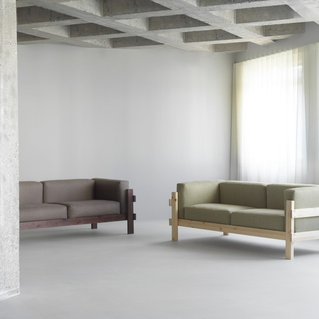 Brown and green sofas with minimalist designs, set against a light gray background and bright, sheer curtains.
