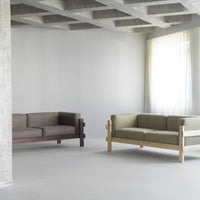 Brown and green sofas with minimalist designs, set against a light gray background and bright, sheer curtains.